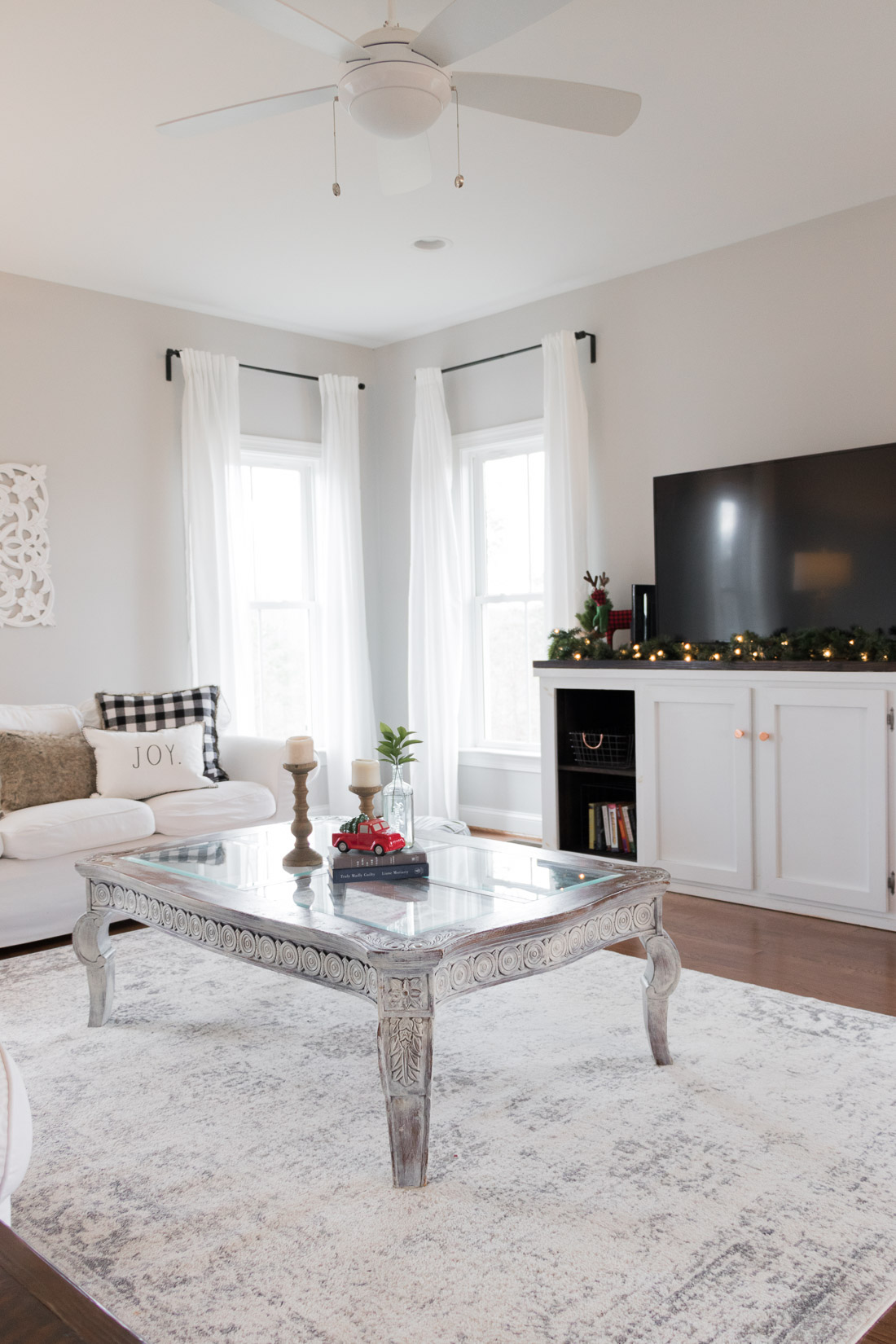 Holiday home tour, holiday decorations in a white decor living room. Lighted garland, white rug, plaid pillows. 