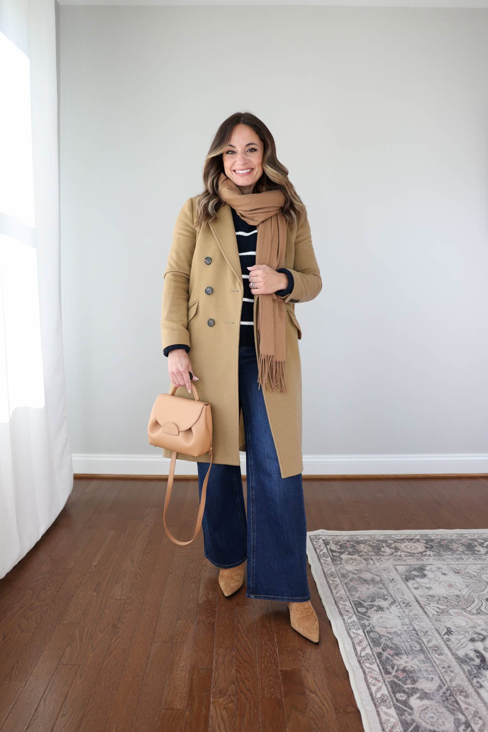 Petite style blogger Brooke of Pumps and Push-Ups styling wide-leg jeans for winter with a camel topcoat, ivory and navy cotton sweater, and a camel scarf— a cozy, and petite-friendly cold-weather outfit idea.
