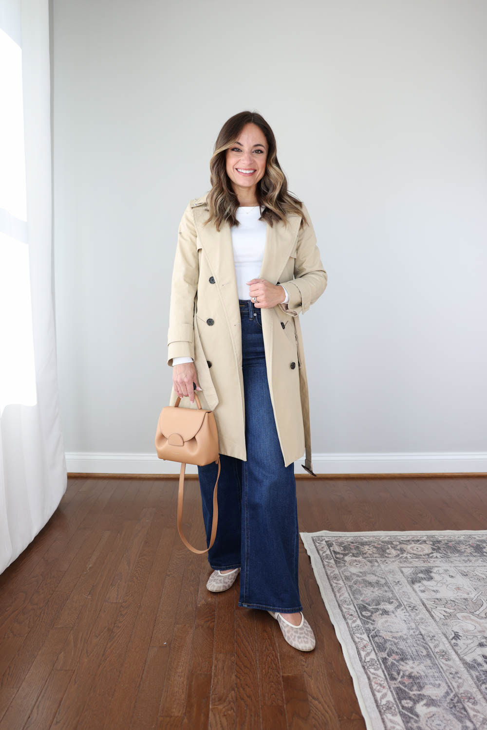 Petite style blogger Brooke of Pumps and Push-Ups styling wide-leg jeans for spring with a white long sleeve top, trench coat, and mesh leopard ballet flats. 